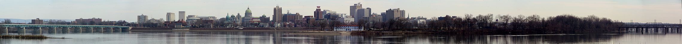 A city skyline, including the Pennsylvania State Capitol, beyond a river with bridges extending across the river on both sides of the photograph. An island is prominent in the right mid-ground.